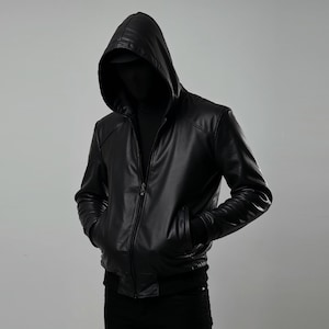 May include: Black leather hooded jacket with a zip-up front and pockets. The jacket has a sleek, modern design, suitable for a casual or edgy look. The hood is up, obscuring the face, adding an air of mystery.