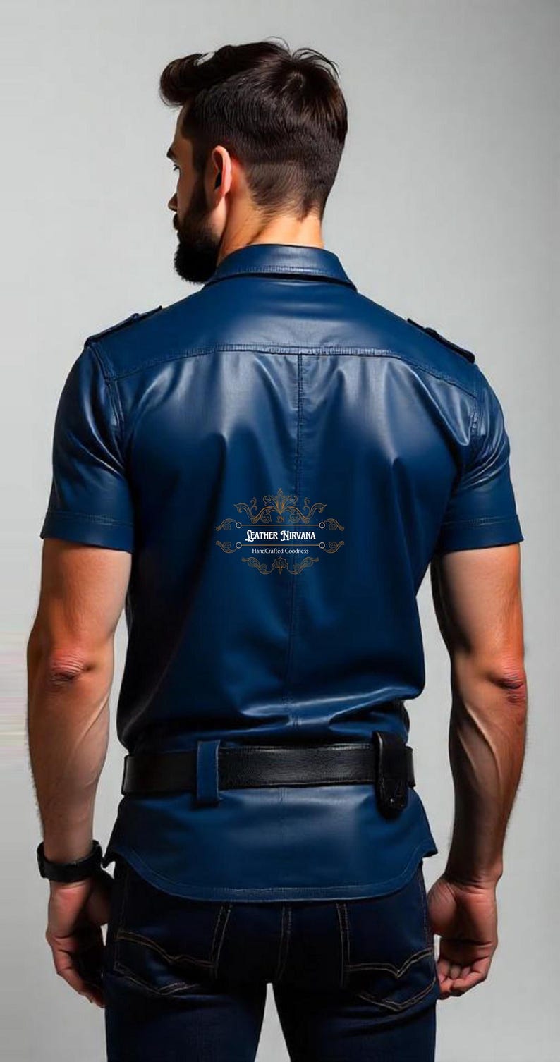 May include: A short-sleeved, navy blue leather shirt with a black belt and dark blue jeans. The shirt has a button-down collar and epaulets. The back of the shirt features the gold text "LEATHER NIRVANA HandCrafted Goodness".