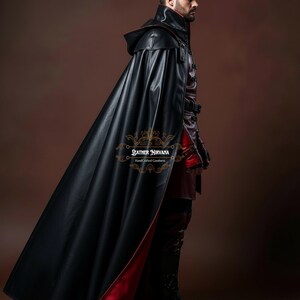 May include: A black leather cape with a red lining, worn over a matching outfit. The cape has a hood and is part of a costume. The image includes the text "Leather Nirvana Handcrafted Goodness".