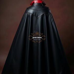 May include: A black leather cape with a red collar and a devil horn headpiece. The cape has a long, flowing design and a decorative emblem near the bottom. The cape is made of a shiny, smooth material.
