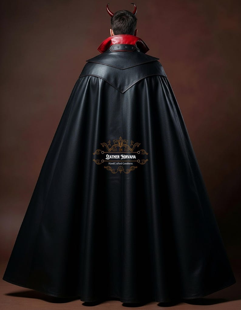 May include: A black leather cape with a red collar and a devil horn headpiece. The cape has a long, flowing design and a decorative emblem near the bottom. The cape is made of a shiny, smooth material.