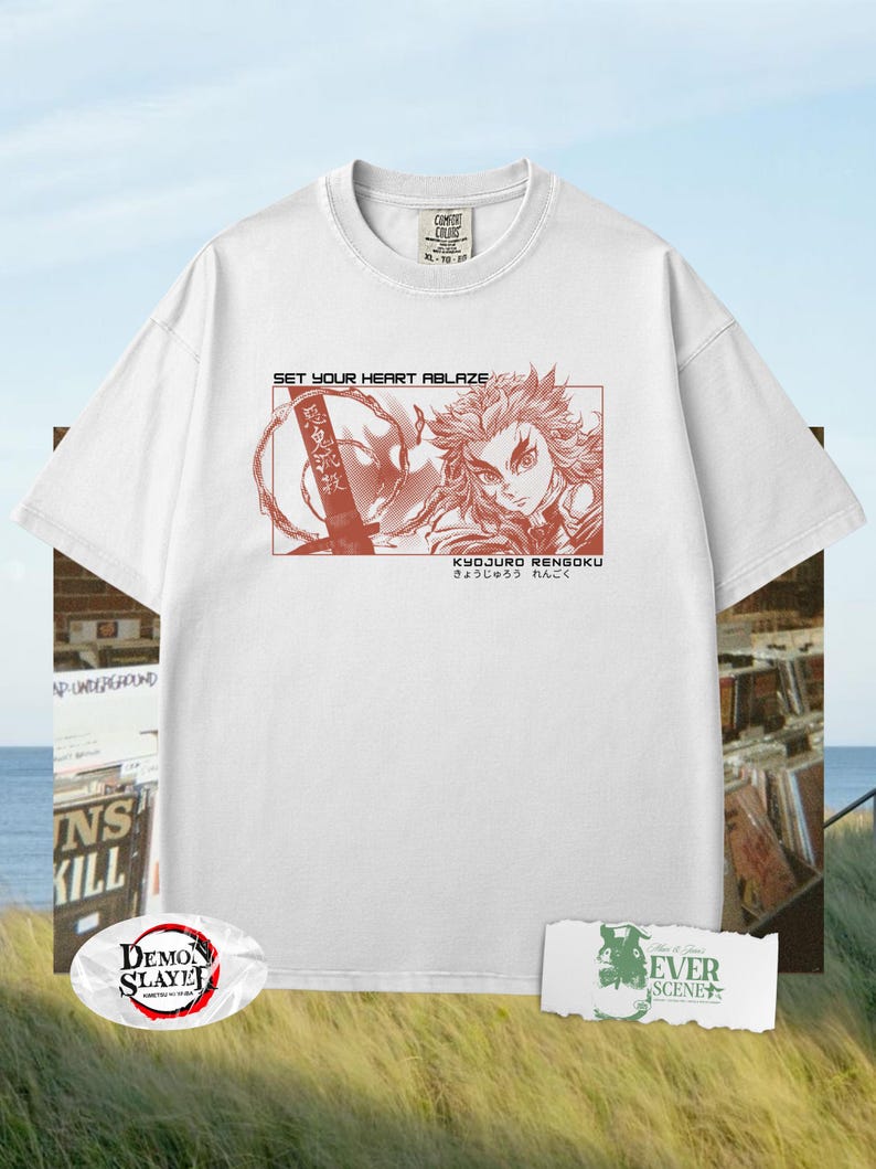 May include: White t-shirt featuring a red graphic of a character from the anime series Demon Slayer. The graphic includes the text "SET YOUR HEART ABLAZE" and Japanese text. The shirt has a crew neck and short sleeves.