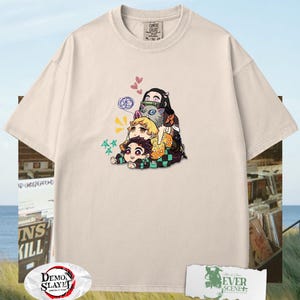 Peut inclure: T-shirt cr&egrave;me avec un graphisme de personnages d'anime empil&eacute;s les uns sur les autres. Le design comprend des c&oelig;urs, des &eacute;toiles et d'autres d&eacute;tails. Le t-shirt a un col rond et des manches courtes. Le texte "Demon Slayer" est visible sur un logo.