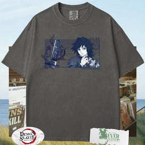 May include: Charcoal grey t-shirt with a rectangular graphic of an anime character with dark hair and a sword. The text "TOMIOKA GIYU" is below the graphic. The shirt has a crew neck and short sleeves. The shirt also has the text "COMFORT COLORS" on the tag.