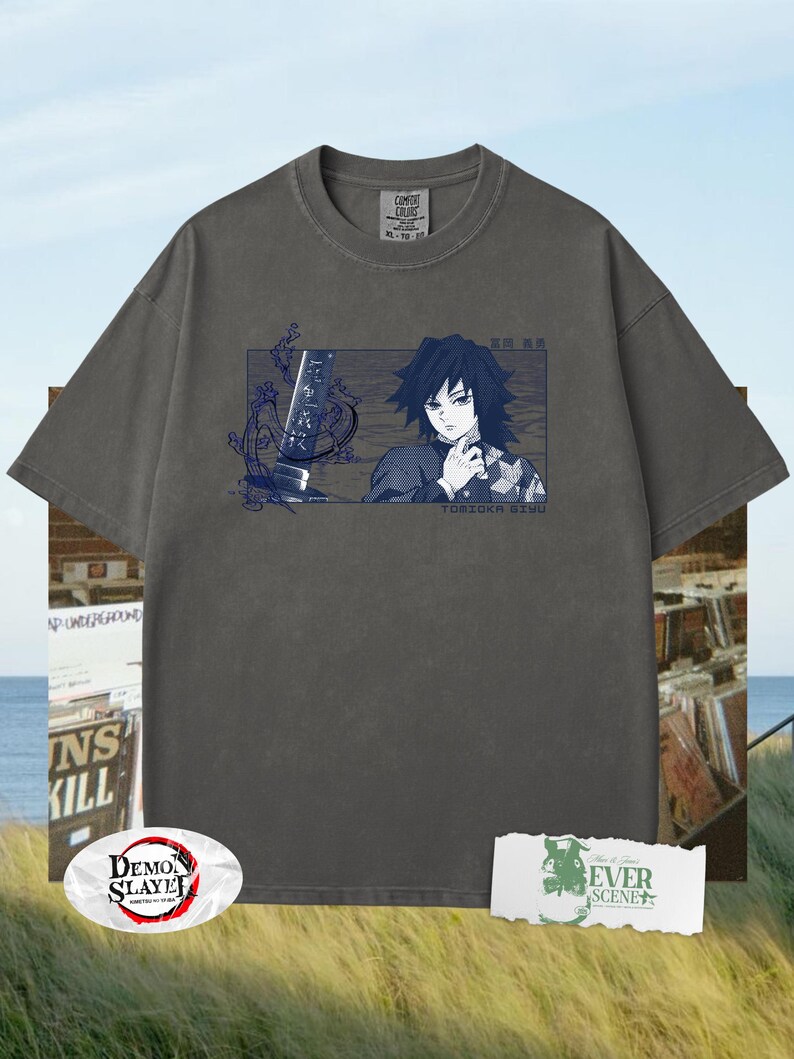 May include: Charcoal grey t-shirt with a rectangular graphic of an anime character with dark hair and a sword. The text "TOMIOKA GIYU" is below the graphic. The shirt has a crew neck and short sleeves. The shirt also has the text "COMFORT COLORS" on the tag.