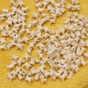 Könnte beinhalten: Eine Ansammlung kleiner, cremefarbener, knochenförmiger Objekte auf einem gelben, strukturierten Hintergrund. Die Objekte scheinen Miniaturwirbel zu sein, möglicherweise für Bastelarbeiten oder Bildungszwecke. Die Beleuchtung ist weich und hebt die Details hervor.