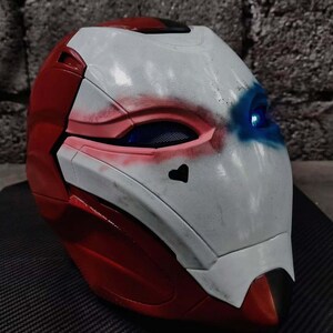 Op de afbeelding: Een rood, wit en blauw helm met een hartsymbool. De helm heeft een ontwerp met rood en wit aan de zijkanten en bovenkant, en wit met rode en blauwe accenten op het gezicht. De oogopeningen hebben een blauwe gloed.