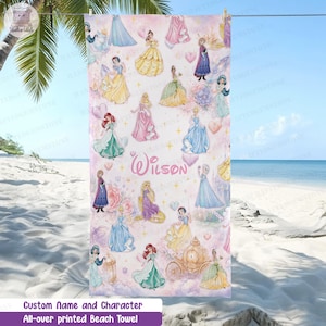 Puede incluir: Una toalla de playa rectangular con un patr&oacute;n repetitivo de varias princesas animadas con vestidos coloridos, un carruaje dorado y corazones sobre un fondo rosa claro. El nombre Wilson est&aacute; impreso en letra cursiva rosa en el centro.