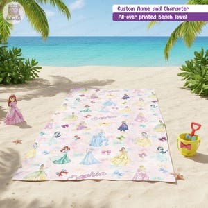 Puede incluir: Una toalla de playa rectangular con un estampado integral de varias princesas de dibujos animados con vestidos coloridos, lazos y el nombre Sophia escrito en cursiva. La toalla est&aacute; extendida sobre una playa de arena con un cubo.