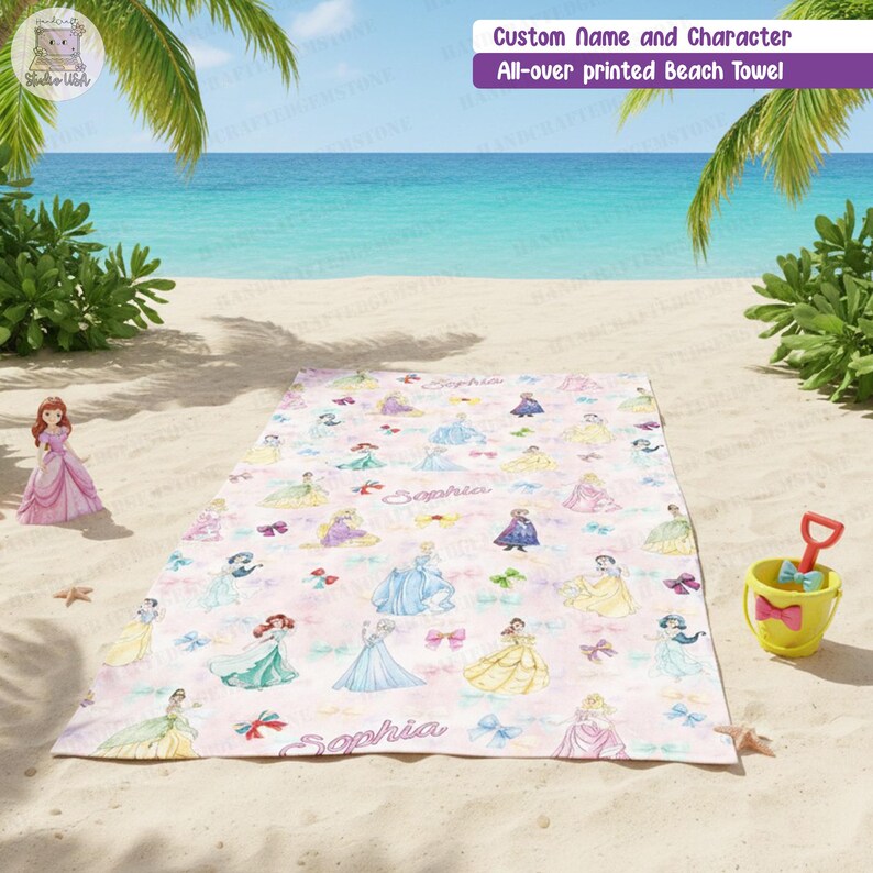 Puede incluir: Una toalla de playa rectangular con un estampado integral de varias princesas de dibujos animados con vestidos coloridos, lazos y el nombre Sophia escrito en cursiva. La toalla est&aacute; extendida sobre una playa de arena con un cubo.