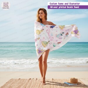 Puede incluir: Una toalla de playa blanca con un estampado integral de varias princesas de dibujos animados y corazones rosas. La toalla muestra el nombre personalizado Dulcie en una fuente cursiva rosa estilizada. La tela es ligera y rectangular.