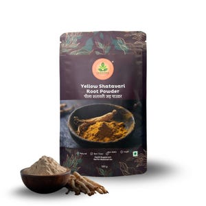Op de afbeelding: Een verpakking Yellow Shatavari Root Powder met tekst in het Engels en Hindi. Een houten kom bevat geel poeder en een andere kom bevat een bruin poeder. Er zijn ook verschillende stukken wortel zichtbaar.