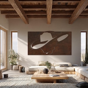 May include: A large, rectangular metal wall art piece featuring a cowboy hat silhouette. The artwork is a warm, rusty brown colour, with a lighter, reflective area within the hat's shape. The piece is mounted on a neutral-coloured wall in a modern living room.