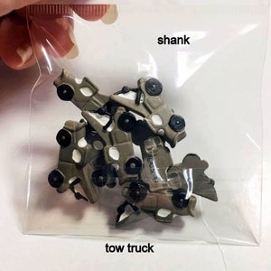 May include: A bag of small, green plastic toy tow trucks with black wheels. The bag has the words "shank" and "tow truck" printed on it.