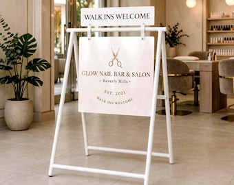 May include: A white A-frame metal sign stand featuring a rectangular top sign reading WALK INS WELCOME and a larger square sign below with a rose gold scissor icon, the text GLOW NAIL BAR & SALON, Beverly Hills, EST. 2021, and WALK INS WELCOME.