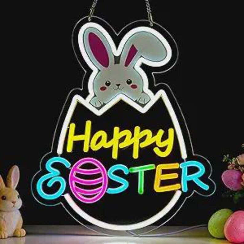 May include: A neon sign in the shape of an egg with a bunny peeking out. The sign says "Happy Easter" in colorful neon lettering. A small bunny figurine and Easter eggs are visible in the foreground.