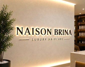 May include: A wall-mounted sign featuring the black text NAISON BRINA LUXURY HAIRCARE with backlighting that creates a glowing effect against a light-colored wall. A green potted plant is positioned to the left of the illuminated signage.