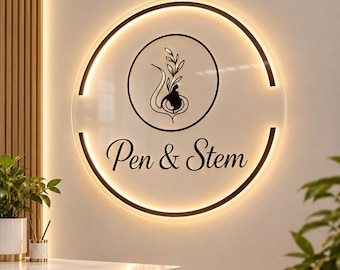 May include: A circular wall sign featuring a backlit edge and a central black graphic of a stylized plant stem. The text Pen & Stem is printed in a black script font below the graphic. The sign has a smooth, light-colored surface finish.