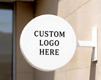 May include: A circular white wall-mounted sign featuring the black text CUSTOM LOGO HERE. The sign is attached to a matching white metal bracket that extends from the side, providing a clean and professional display for branding purposes.