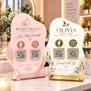 May include: Two irregular-shaped acrylic signs with gold stands. The left sign is pink with Blush & Bloom Beauty Studio branding, Facebook and Instagram icons, and QR codes. The right sign is white with Olivia Nail Bar branding and similar icons.