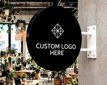 May include: A circular black wall-mounted sign featuring a white geometric diamond logo and the text CUSTOM LOGO HERE. The sign is attached to a concrete pillar with a white metal bracket, displaying a clean, modern design for business branding.