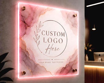 May include: A square acrylic sign with a pink and white marble pattern, illuminated by a glowing neon border. The center features a circular frame with a leaf branch, the text CUSTOM LOGO Here, and the phrase YOUR BRAND. OUR PASSION. mounted with four gold standoffs.