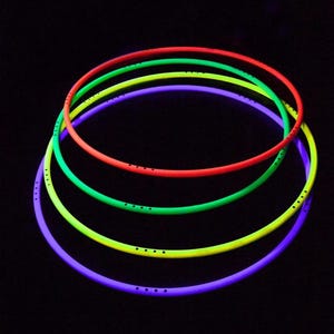Op de afbeelding: Vier cirkelvormige hoepels in levendige neonkleuren, waaronder rood, groen, geel en paars. Elke hoepel is voorzien van een reeks kleine, gelijkmatig verdeelde zwarte stippen langs de omtrek, gerangschikt in groepjes van vier op een zwarte achtergrond.