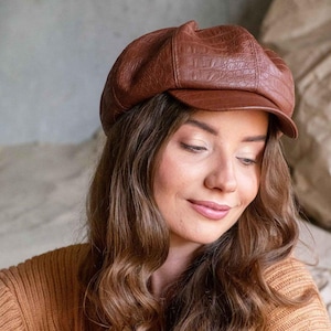 Peut inclure: Casquette de style gavroche marron avec une texture imitant le cuir et une petite visière. La casquette est de couleur marron chaud et terreux. Un accessoire de mode.