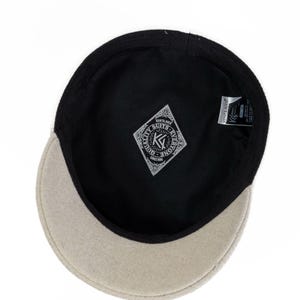 May include: A cap with a beige brim and a black interior lining. The interior features a diamond-shaped patch with the text KENTA AVER, QUALITY SUITS EVERYONE, and SINCE 1995. A small white tag with black text is attached to the inner rim.