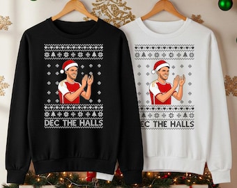 Könnte beinhalten: Zwei Weihnachtspullover, einer schwarz und einer weiß, mit festlichem Design. Jeder zeigt eine Person mit Weihnachtsmütze, die klatscht, umgeben von Schneeflocken und Weihnachtsmotiven. Der Text "DEC THE HALLS" ist auf dem schwarzen Pullover aufgedruckt.