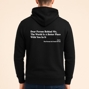 Könnte beinhalten: Schwarzer Kapuzenpullover mit dem weißen Text: "Dear Person Behind Me, The World Is A Better Place With You In It. Love, The Person In Front Of You". Der Hoodie hat eine Kapuze und einen Kordelzug.