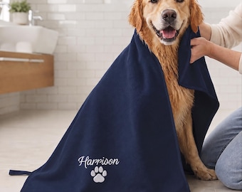 Könnte beinhalten: Ein dunkelblaues Haustierhandtuch mit dem in Weiß gestickten Namen Harrison über einer weißen Pfotenabdruck-Grafik. Das rechteckige Handtuch ist über einen goldfarbenen Hund drapiert und zeigt eine weiche Stoffstruktur sowie eine kleine Stoffschlaufe.