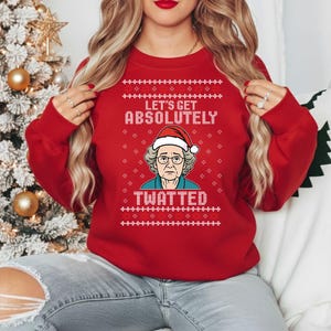 Może przedstawiać: Czerwony świąteczny sweter z napisem "LET'S GET ABSOLUTELY TWATTED" i grafiką kobiety w czapce Świętego Mikołaja. Sweter ma świąteczny wzór płatków śniegu.