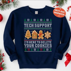 May include: Navy blue sweatshirt with a festive design. The text "TECH SUPPORT" is above the phrase "I'M HERE TO DELETE YOUR COOKIES". The design includes gingerbread cookies and snowflakes.