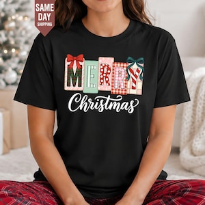 Könnte beinhalten: Ein schwarzes T-Shirt mit kurzen Ärmeln, das das Wort MERRY in bunten, gemusterten Blockbuchstaben mit Schleifen zeigt, sowie das Wort Christmas in weißer Schreibschrift darunter. Die Buchstaben haben Karomuster, Streifen und Punkte.