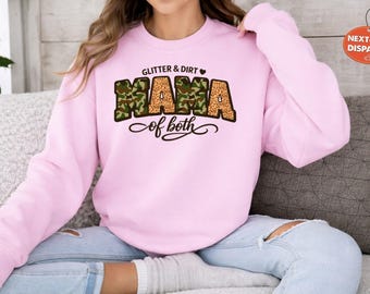 Könnte beinhalten: Ein hellrosa Sweatshirt mit dem Text "Glitter & Dirt Mama of both". Das Wort "Mama" ist in einem Tarn- und Leopardenmuster gestaltet. Das Sweatshirt ist ein langärmeliger Rundhalsausschnitt.