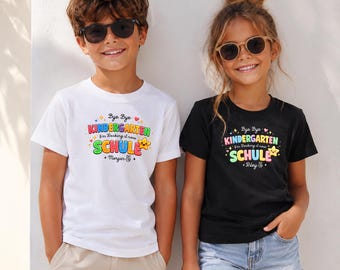 Könnte beinhalten: Ein weißes T-Shirt und ein schwarzes T-Shirt, jeweils mit einem bunten Grafikdruck mit der Aufschrift Bye Bye KINDERGARTEN I'm Rocking it now SCHULE, einem Sternsymbol und einem Namen. Das weiße Shirt zeigt Morgan, das schwarze Riley.