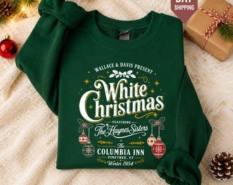 Könnte beinhalten: Ein dunkelgrünes Sweatshirt mit Rundhalsausschnitt und einem weiß-goldenen Grafikdruck mit der Aufschrift Wallace & Davis Present White Christmas Featuring The Haynes Sisters The Columbia Inn Pinetree, VT Winter 1954, verziert mit Weihnachtskugeln.