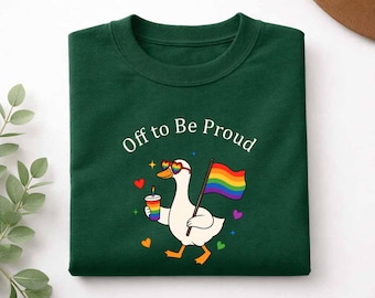 May include: A dark green crewneck sweatshirt featuring a graphic of a white duck wearing rainbow heart-shaped sunglasses, holding a rainbow-striped cup and a rainbow flag. The text "Off to Be Proud" is printed above the duck with small hearts.