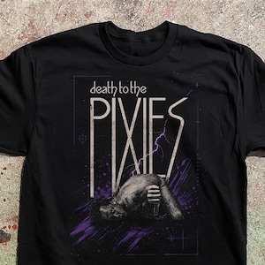 Puede incluir: Una camiseta negra de manga corta con un estampado gráfico que incluye el texto "death to the PIXIES" en letras blancas. El diseño presenta una ilustración punteada de una figura acostada, acentuada por rayos púrpuras y trazos abstractos.
