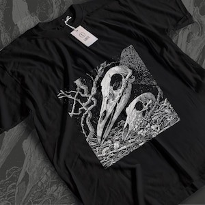 Puede incluir: Camiseta negra con un gráfico blanco detallado de dos cráneos de aves y ramas intrincadas y retorcidas. El diseño está centrado en la camiseta, con una etiqueta que dice "LARGE". La estética general es gótica e inspirada en la naturaleza.