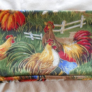 May include: A green fabric with a repeating pattern of roosters and pumpkins. The roosters are brown, yellow, red, and blue. The pumpkins are orange and yellow.