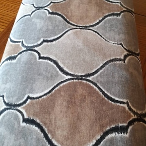 May include: A fabric with a repeating pattern of brown and gray teardrop shapes outlined in black. The fabric has a textured surface.