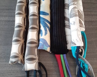 May include: A collection of six cat toys. Each toy is a rectangular shape with a different patterned fabric. Some have dangling ribbons and bells attached. The fabrics include geometric, floral, and solid black.