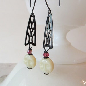 May include: A pair of dangle earrings with black filigree metal charms and white faceted beads. The beads are accented with small pink beads.