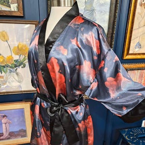 May include: A silky, dark blue robe with a red floral pattern and black trim. The robe is tied with a black sash. The robe is displayed on a mannequin.
