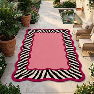 May include: A rectangular area rug featuring a solid pink centre, a scalloped border, and a black and white zebra stripe pattern. The rug has a thick, vibrant pink trim that outlines the wavy edges, creating a distinct contrast against the striped design.