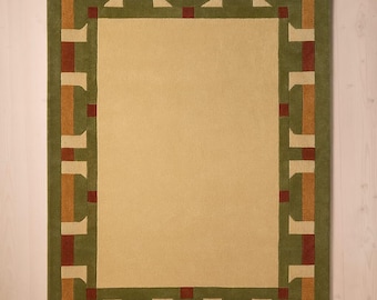 May include: Rectangular area rug with a central beige field and a border in shades of green, brown, and red. The border features a geometric pattern of rectangles and squares. The rug is placed on a light-colored wooden floor.