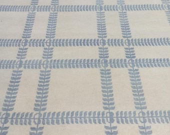 May include: A rectangular rug with a cream-colored background and a repeating pattern of light blue leaf-like designs. The pattern creates a grid-like structure across the rug's surface. The rug is made of a soft, woven material.