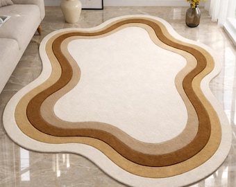 Puede incluir: Una alfombra crema con bordes ondulados y bandas concéntricas marrones y beige. La forma única de la alfombra y su paleta de colores neutros la convierten en una adición elegante a cualquier espacio habitable. La alfombra está hecha de un material suave y afelpado.